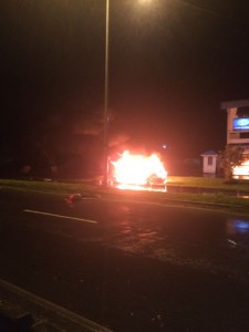 The burning car in which Bashment was travelling. In the foreground is his body.