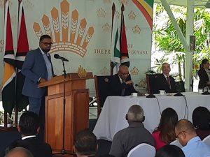 President Irfaan Ally at lectern seated are Vice President Bharrat Jagdeo and Chief Executive Officer of Hess Corporation, John Hess.